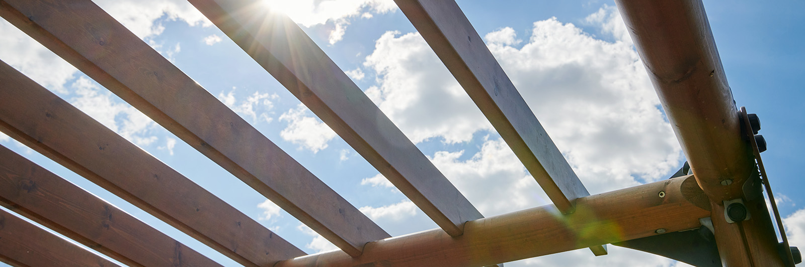 Blick in den Himmel aus dem Inneren einer Pergola, so dass man die Holzlatten an der Spitze sehen kann.